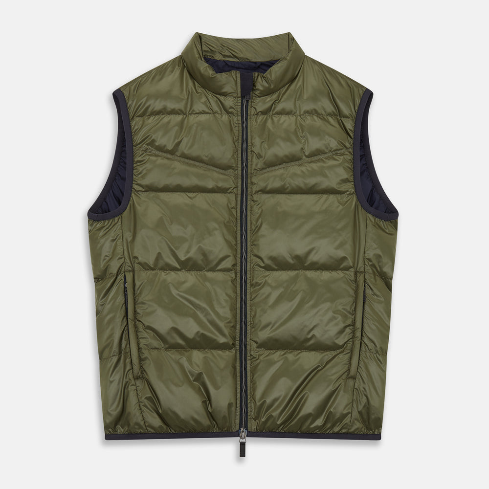 A man stands against a plain background wearing the Turnbull & Asser Green Peyton Sealup Quilted Gilet over a striped shirt, dark trousers, and white sneakers, with his hands in his pockets and looking slightly to the side.