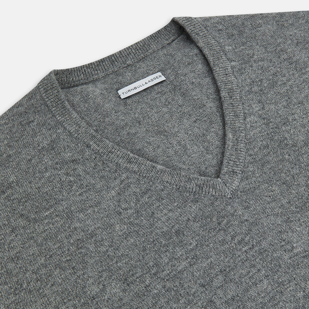 The Turnbull & Asser Grey Melange Cashmere V-neck Jumper features long sleeves, ribbed cuffs and hem, showcasing timeless style against a white background.
