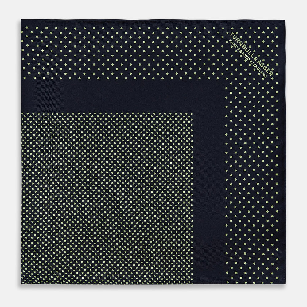 The Turnbull & Asser Navy and Melon Green Dot Silk Pocket Square features small melon green dots on navy silk with a solid border. One corner is folded over to highlight its exquisite handmade craftsmanship.