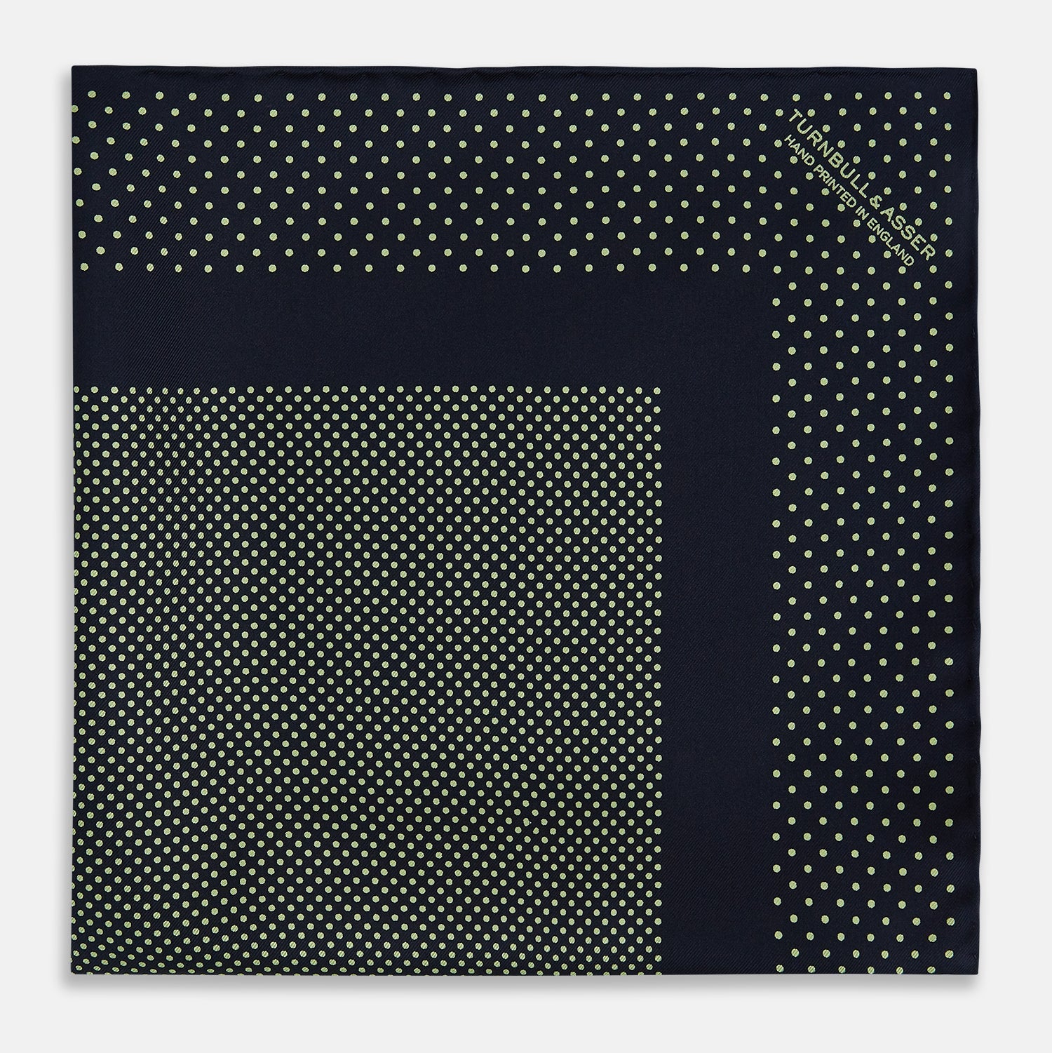 View 3 of product The Turnbull & Asser Navy and Melon Green Dot Silk Pocket Square features small melon green dots on navy silk with a solid border. One corner is folded over to highlight its exquisite handmade craftsmanship.