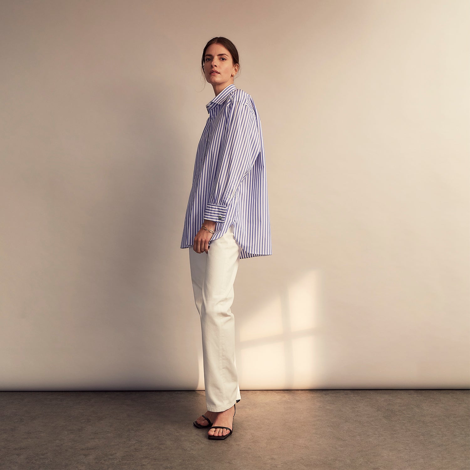 View 9 of product The Turnbull & Asser Pale Blue Candy Stripe Cotton Marlene Shirt is an oversized women's collared shirt with long sleeves, buttoned cuffs, and vertical blue and white stripes, shown laid flat on a white background.