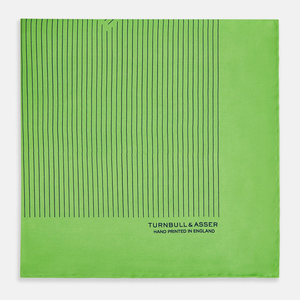 The Fern Green Stripe Silk Pocket Square by Turnbull & Asser features thin black vertical stripes, celebrates British heritage, and is inscribed “TURNBULL & ASSER HAND PRINTED IN ENGLAND” in one corner; one corner is folded inward.