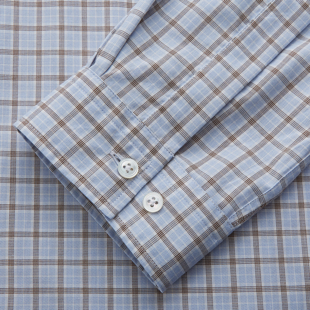 A man wearing glasses and a Pale Blue Multi Check Cashmerello Holiday Fit Winnington Shirt by Turnbull & Asser leans casually against a white countertop, looking at the camera with a neutral expression.