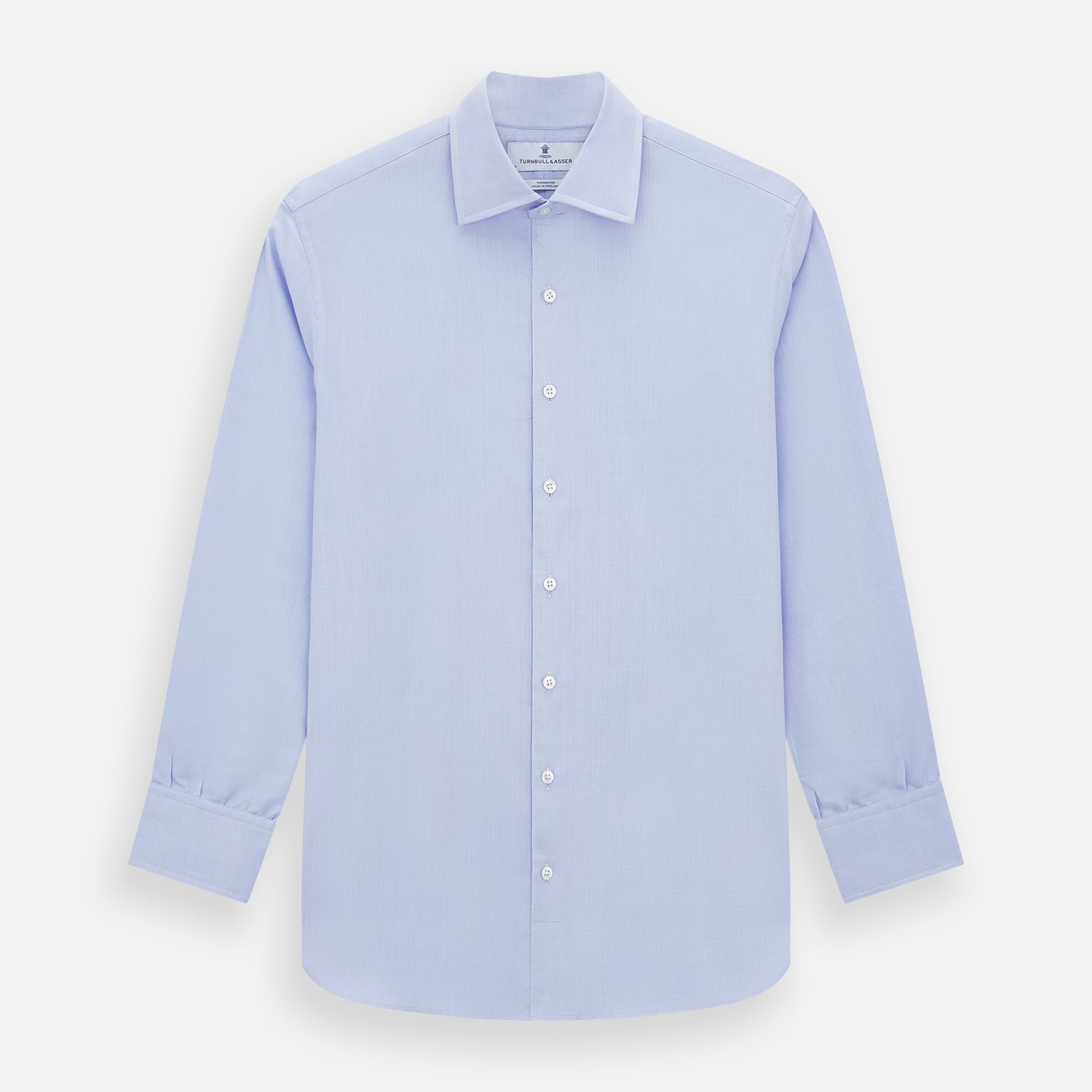 View 1 of product The Turnbull & Asser BLUE HERRINGBONE TAILORED FIT SHIRT WITH KENT COLLAR features long sleeves and buttoned cuffs, offering a timeless formal look in a classic light blue herringbone fabric, laid flat on a white background.