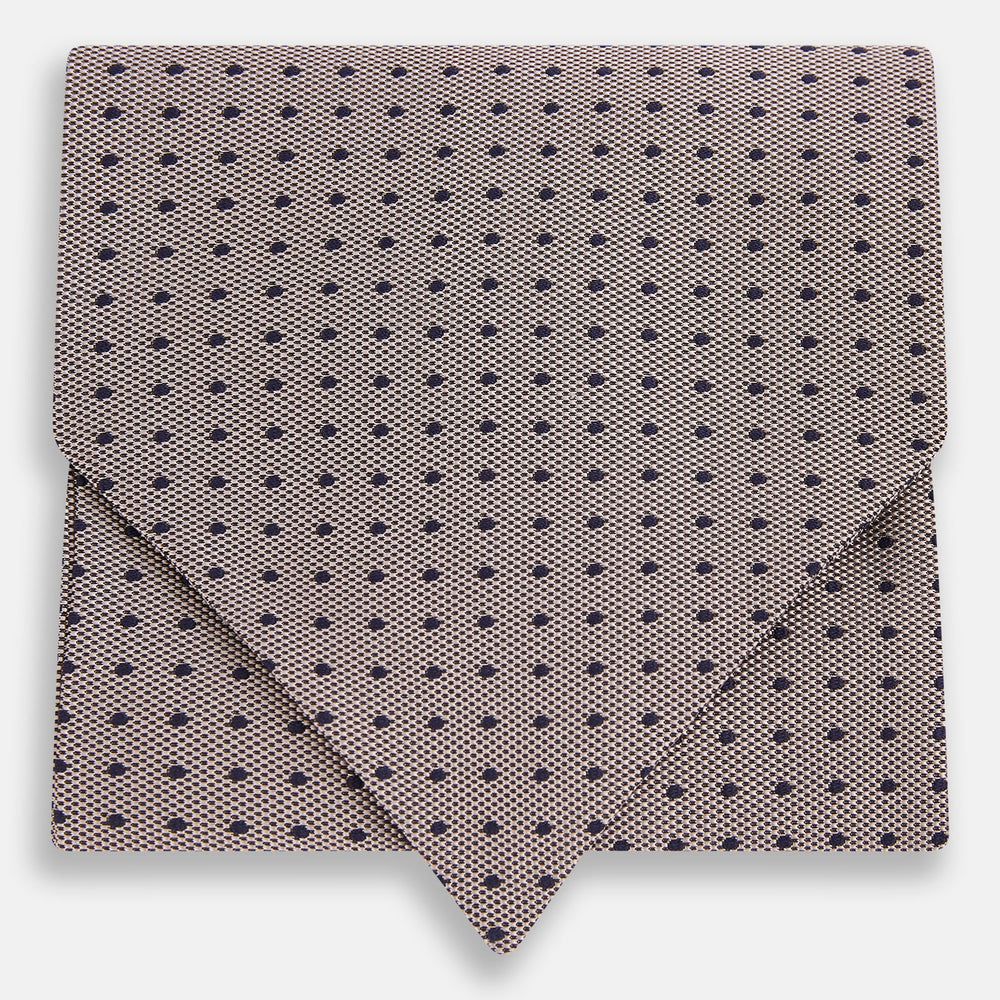 A folded, light-colored pocket square with small dark dots is displayed on a white background. Neatly arranged in a pointed fold, it pairs perfectly with the Turnbull & Asser Lilac and Navy Micro Dot Silk Cravat for an elegant look.