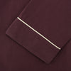 View 3 of product The Turnbull & Asser Plain Plum Silk Modern Pyjama Set, made in England, features white piping, a button-up long-sleeve top with three pockets, and matching pants. The pyjamas are shown against a white background.
