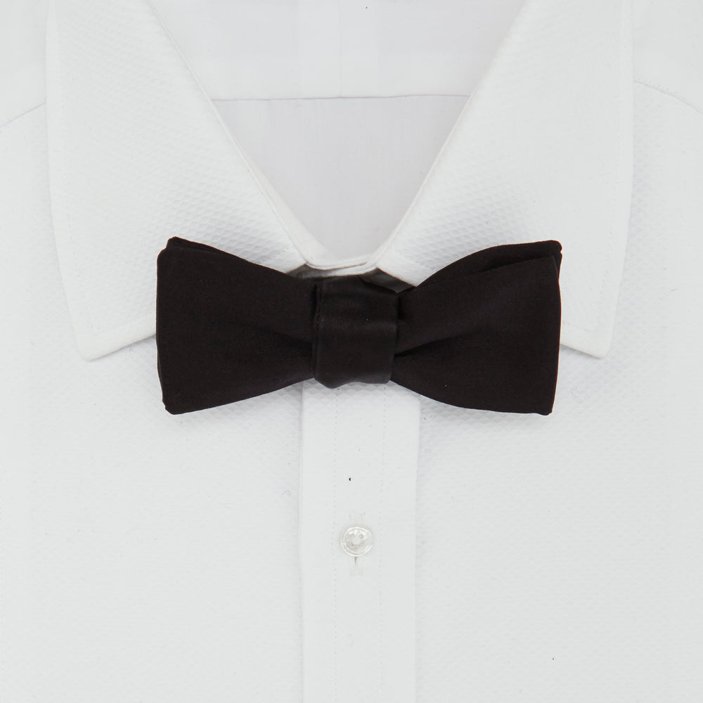 The Turnbull & Asser Black Batwing Satin Bow Tie features a smooth, matte finish and is neatly tied on a plain white background—ideal for formal occasions.