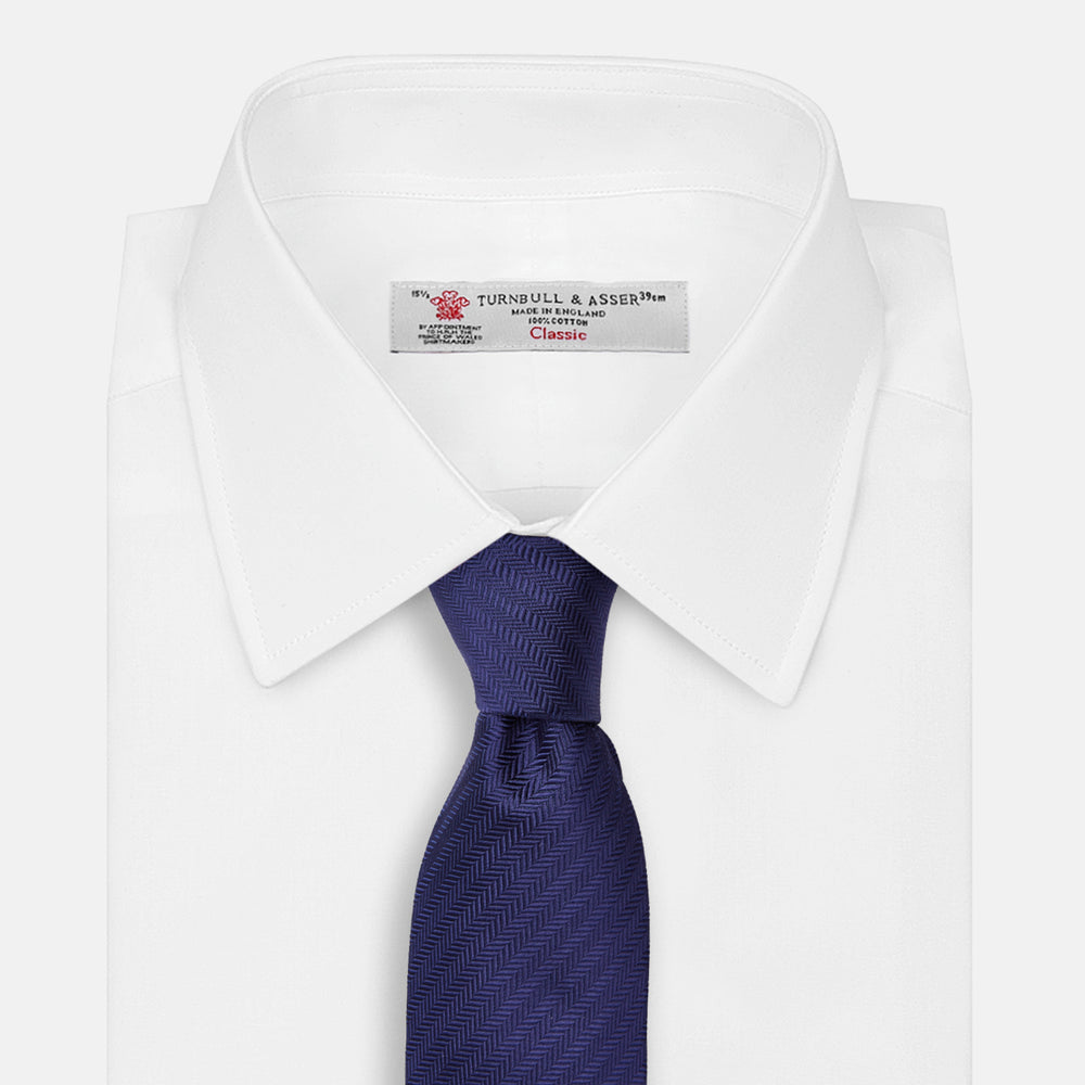 The PLAIN HERRINGBONE NAVY TIE by Turnbull & Asser, crafted from silk with a subtle pattern, is elegantly rolled and displayed against a plain white background.