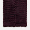 View 4 of product The Turnbull & Asser Knitted Burgundy Square Silk Plain Tie, featuring a textured open-weave pattern, is rolled up and displayed on a plain white background—a versatile accessory for the modern gentleman.