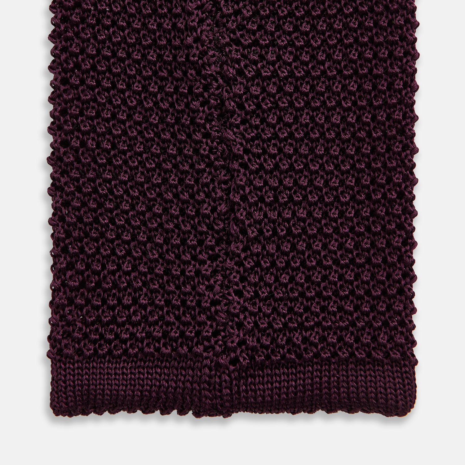 View 4 of product The Turnbull & Asser Knitted Burgundy Square Silk Plain Tie, featuring a textured open-weave pattern, is rolled up and displayed on a plain white background—a versatile accessory for the modern gentleman.