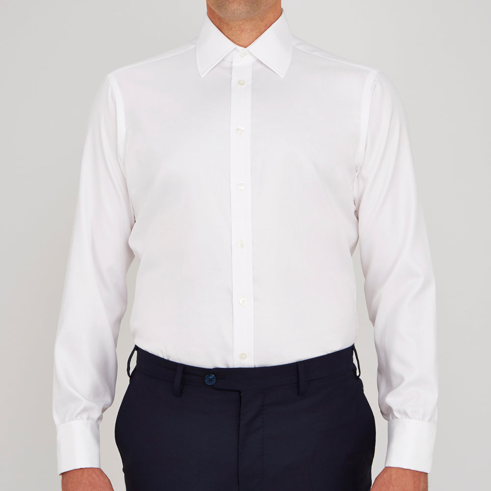 A neatly folded Turnbull & Asser White Oxford Shirt with T&A collar and double cuffs is displayed on a light blue background.