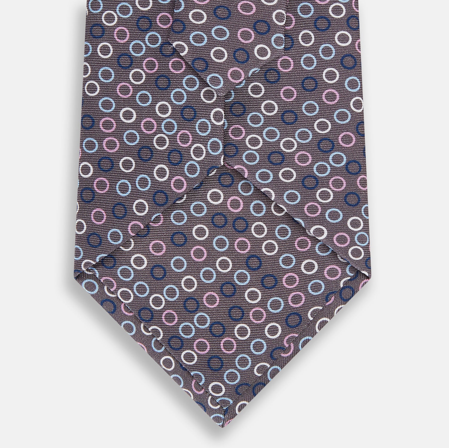 View 3 of product The Turnbull & Asser Purple and Blue Circle Ash Silk Tie features small blue, pink, and white circles on a dark purple background, adding an elegant touch when displayed on a light surface.