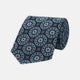 The Jacquard Silk Geometric Tie by Turnbull & Asser features a navy blue base with light blue and white star and circle motifs, shown rolled on a white background.