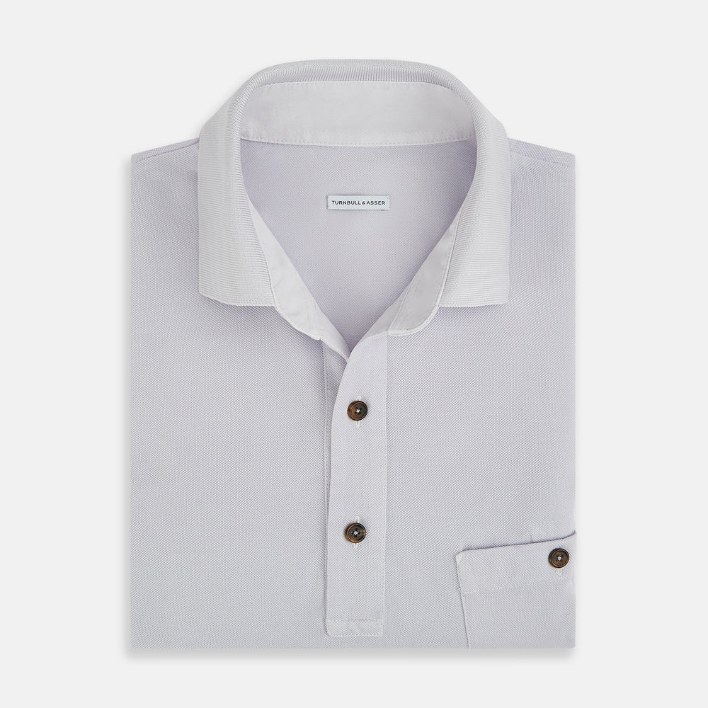 A soft pink cotton polo shirt by Turnbull & Asser features short sleeves, a contrasting white collar, three dark buttons, and a left chest pocket. Laid flat on a white background—it’s perfect for modern men’s fashion.