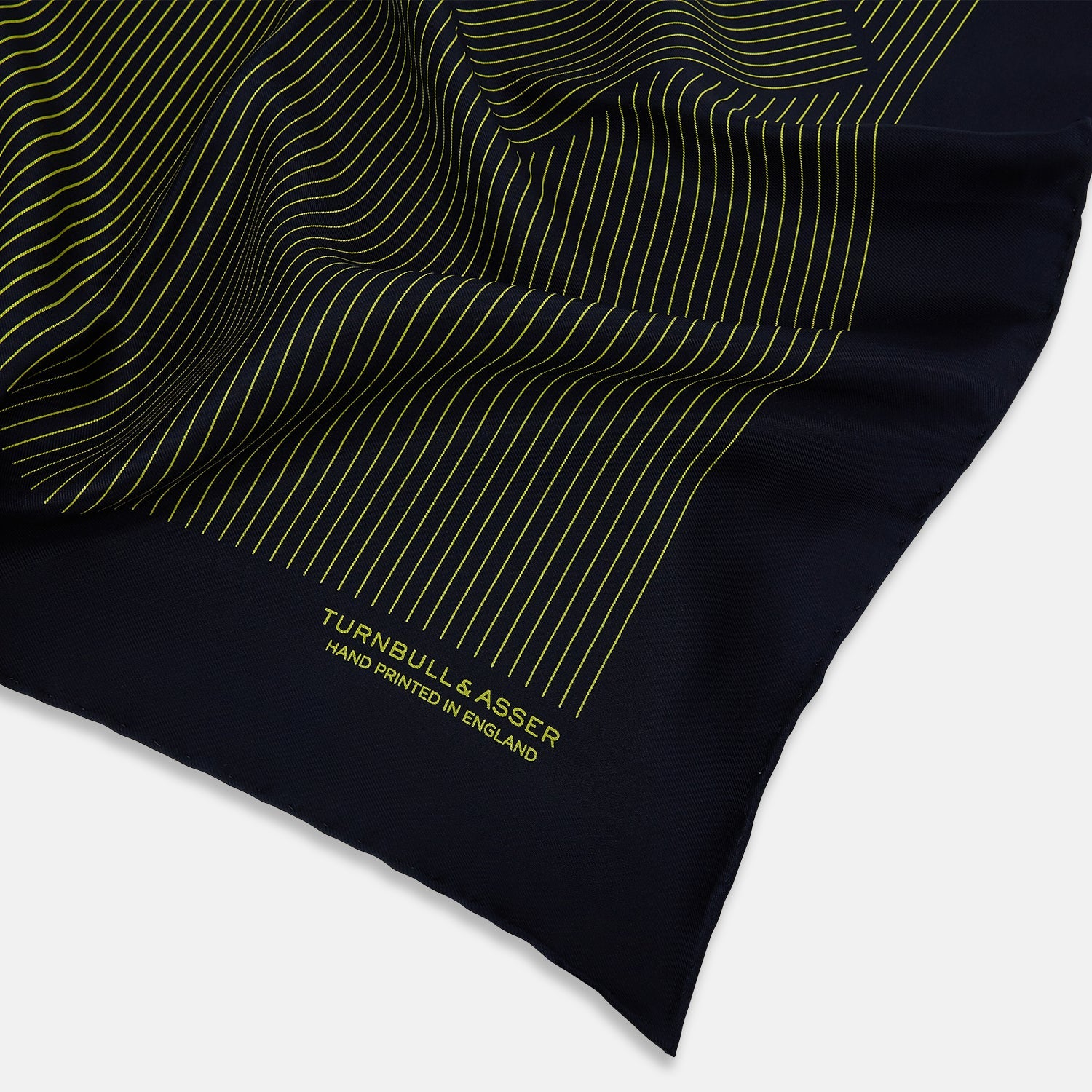 View 2 of product Turnbull & Asser Navy and Yellow Stripe Silk Pocket Square features hand-rolled edges, striped pattern, and "Turnbull & Asser Hand Printed in England" text in yellow on the bottom right corner.