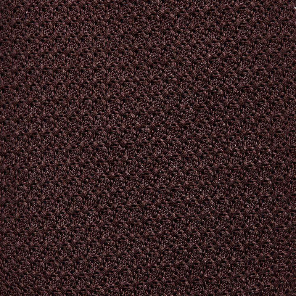 The Turnbull & Asser Ruby Red Knitted Tie, shown rolled-up against a white background, is a textured silk accessory that adds versatile sophistication to any gentleman's wardrobe.
