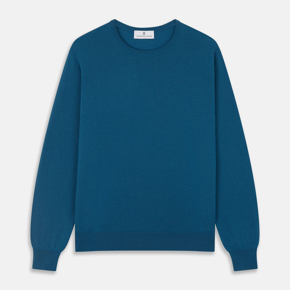 A man with light skin and short brown hair stands against a plain background, wearing the Turnbull & Asser Ocean Blue Merino Kingston Crew Neck Jumper and cream-colored pants, looking directly at the camera with a neutral expression.