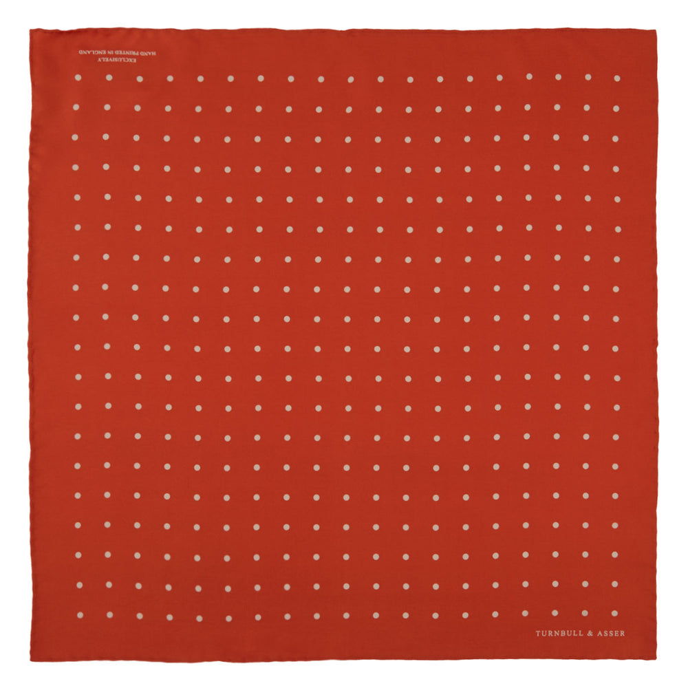 The Orange Spot Silk Pocket Square by Turnbull & Asser features evenly spaced white polka dots and the brand’s name in one corner, making this dapper accessory a standout addition to any outfit.