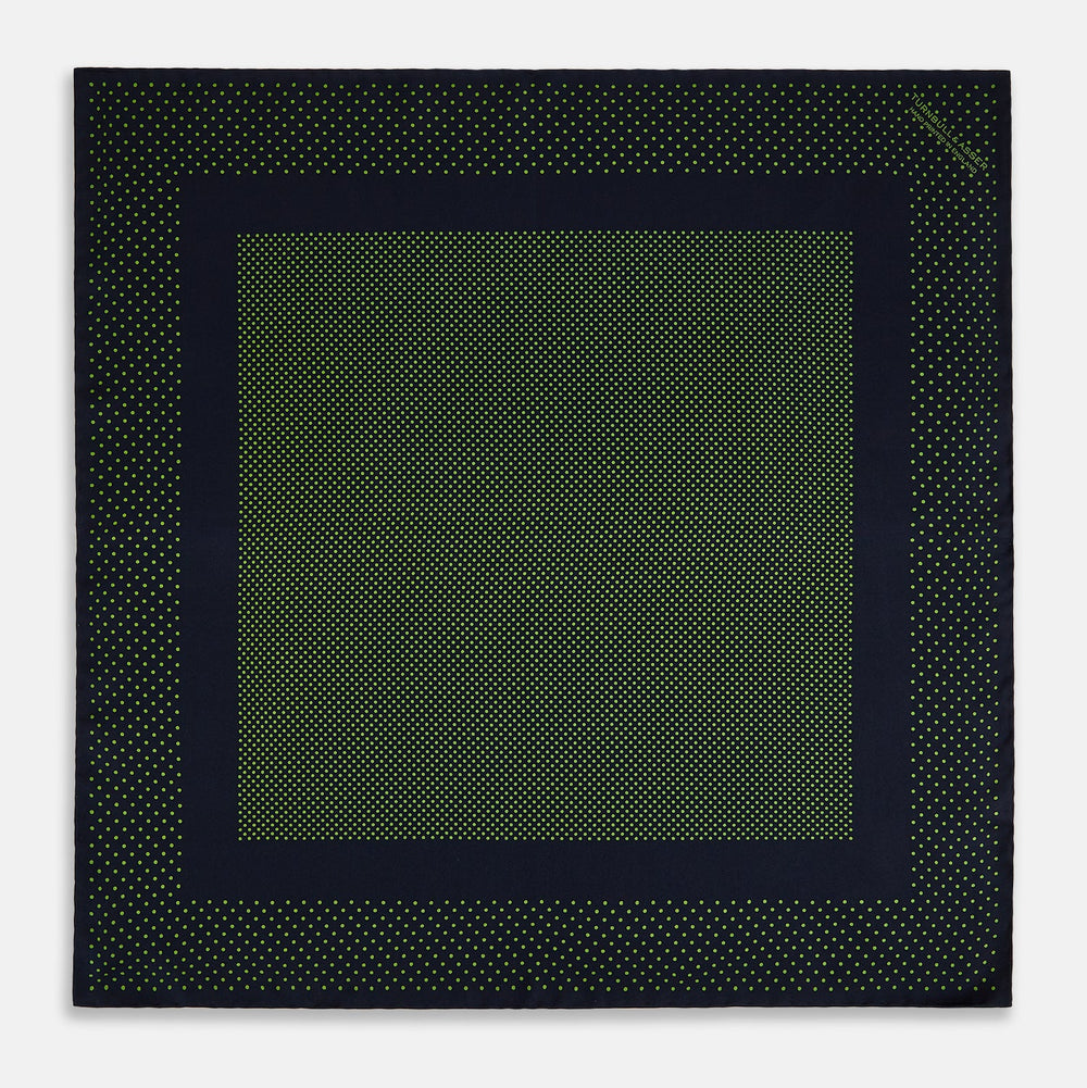 The Turnbull & Asser Navy and Kelly Green Dot Silk Pocket Square features small green dots on navy silk and a folded corner displaying the reverse—an elegant, handmade accessory perfect for enhancing any formal attire.