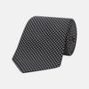 View 1 of product The Turnbull & Asser Black and White Spot Printed Silk Tie, shown neatly rolled on a plain white background, is an essential accessory to elevate any smart attire.