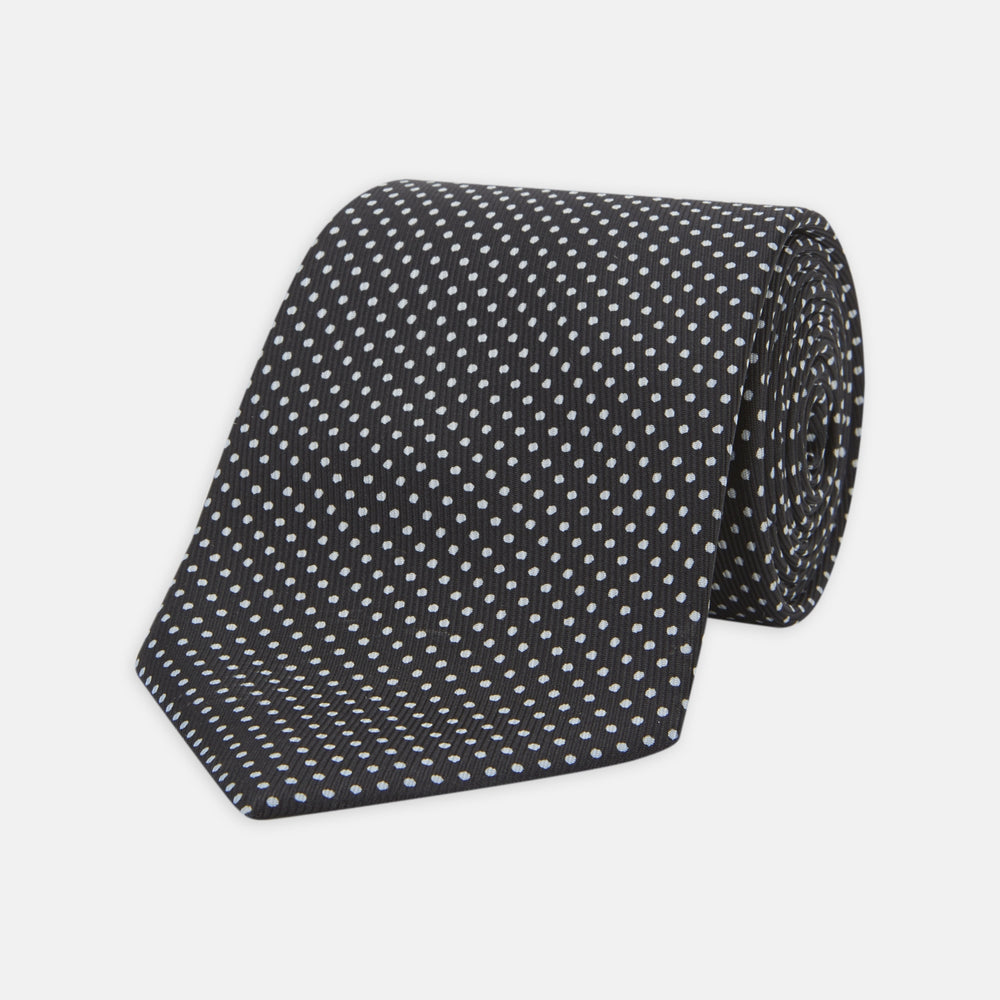 The Turnbull & Asser Black and White Spot Printed Silk Tie, shown neatly rolled on a plain white background, is an essential accessory to elevate any smart attire.
