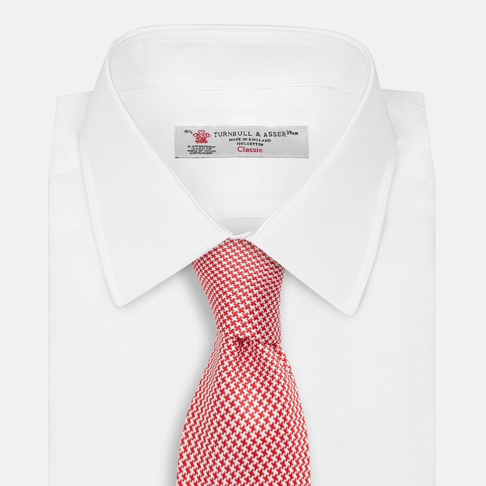 The Turnbull & Asser Red Houndstooth Silk Tie features a textured, small geometric pattern in red and white—ideal as a classic office accessory, shown rolled up on a plain white background.