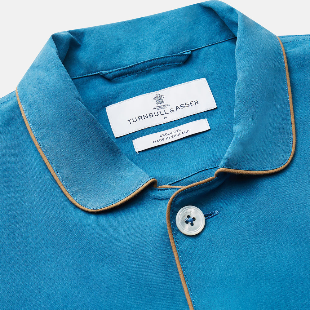 The Turnbull & Asser Blue Silk Hyde Pyjama Set features a modern fit with a long-sleeve button-up top, three pockets, white trim, and elastic-waist pants, all shown on a white background.