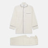 View 1 of product The Cream Pattern Cotton Blend Quin Pyjama Set by Turnbull & Asser features cream stripes, a long-sleeve button-up camp collar shirt with a chest pocket and black piping, and matching drawstring pants.