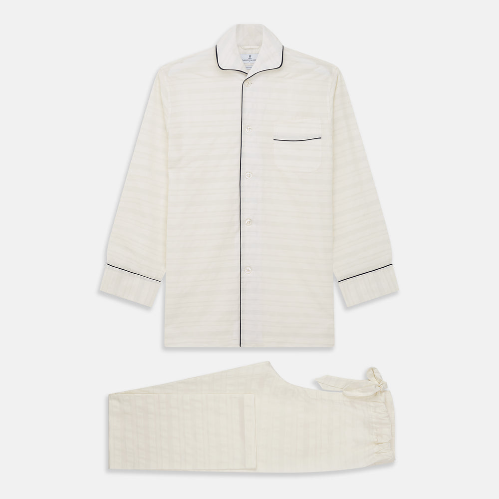 The Cream Pattern Cotton Blend Quin Pyjama Set by Turnbull & Asser features cream stripes, a long-sleeve button-up camp collar shirt with a chest pocket and black piping, and matching drawstring pants.