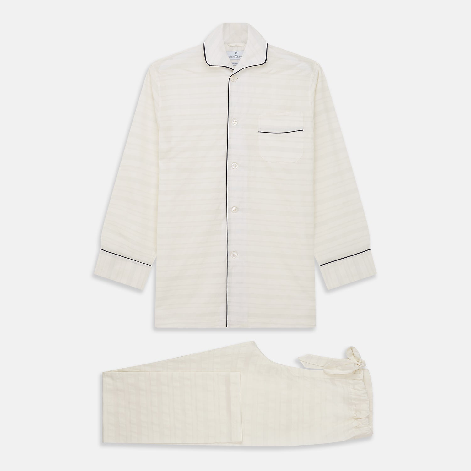 View 1 of product The Cream Pattern Cotton Blend Quin Pyjama Set by Turnbull & Asser features cream stripes, a long-sleeve button-up camp collar shirt with a chest pocket and black piping, and matching drawstring pants.