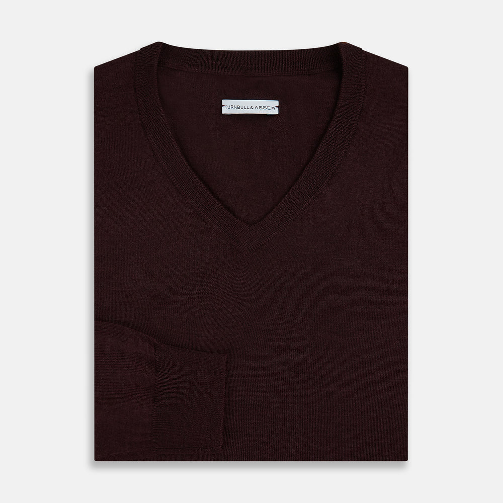 The Turnbull & Asser Burgundy Fine Merino V-Neck Jumper features a classic plain knit design with long sleeves, showcased against a crisp white background.