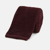 View 1 of product The Turnbull & Asser Knitted Burgundy Square Silk Plain Tie, featuring a textured open-weave pattern, is rolled up and displayed on a plain white background—a versatile accessory for the modern gentleman.