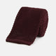 The Turnbull & Asser Knitted Burgundy Square Silk Plain Tie, featuring a textured open-weave pattern, is rolled up and displayed on a plain white background—a versatile accessory for the modern gentleman.