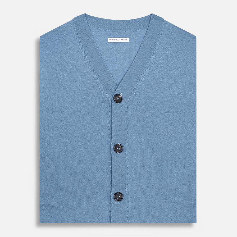 Turnbull & Asser’s Pale Blue Merino V-neck Sleeveless Cardigan features a button-up front, two pockets, and ribbed hem—a classic gentleman’s piece shown on a plain white background.