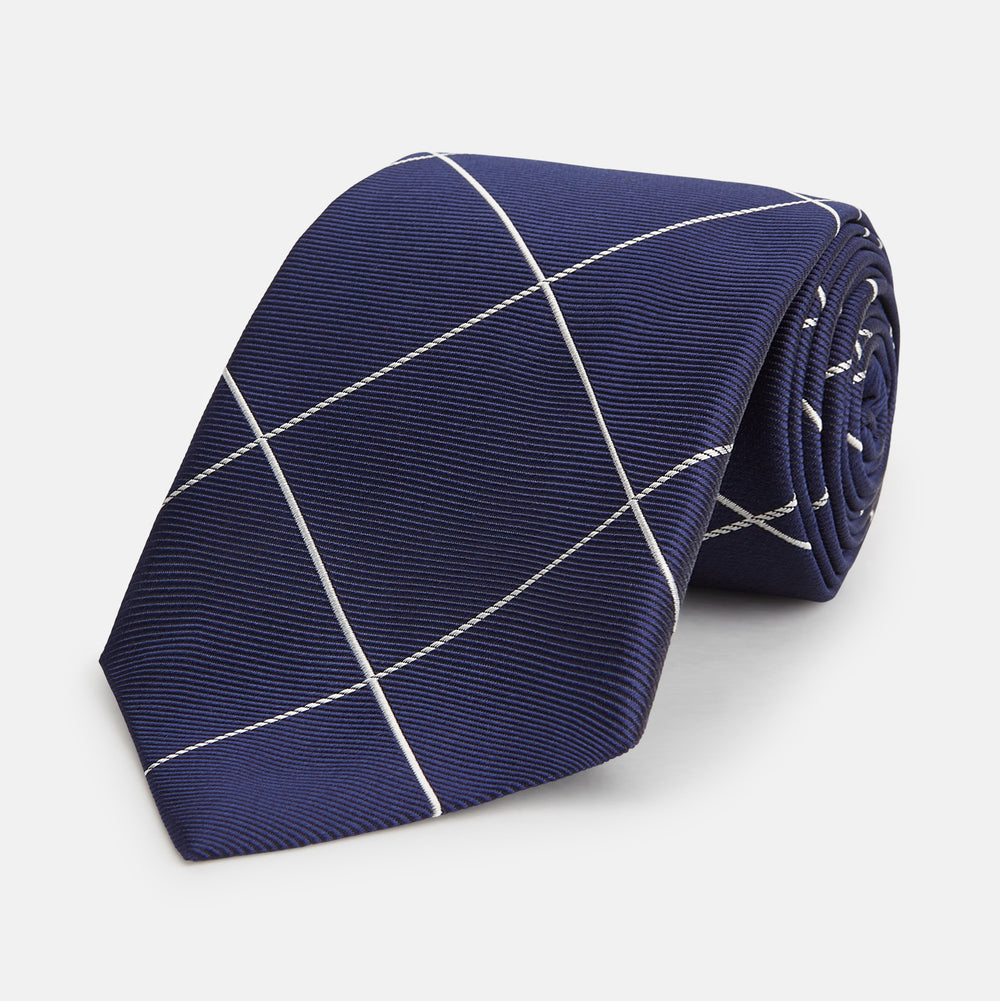 The Turnbull & Asser WINDOW PANE NAVY WHITE TIE features navy blue silk with a subtle diagonal ribbed texture and white windowpane checks, making it the perfect men’s accessory for any formal occasion.