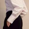 View 7 of product A woman stands in profile, looking down with hands in her pockets, wearing the Turnbull & Asser Turnbull and The Deck White Cotton Expressionist Shirt, paired with high-waisted black-and-white houndstooth pants.