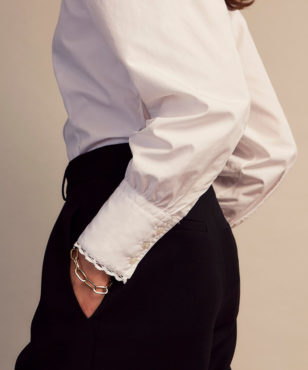 A woman stands in profile, looking down with hands in her pockets, wearing the Turnbull & Asser Turnbull and The Deck White Cotton Expressionist Shirt, paired with high-waisted black-and-white houndstooth pants.