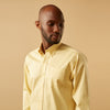 View 2 of product A man stands facing forward against a beige background, wearing the Turnbull & Asser Yellow Piece Dyed Weekend Fit Suffolk Shirt with a Dorset collar, paired with dark jeans and black shoes.