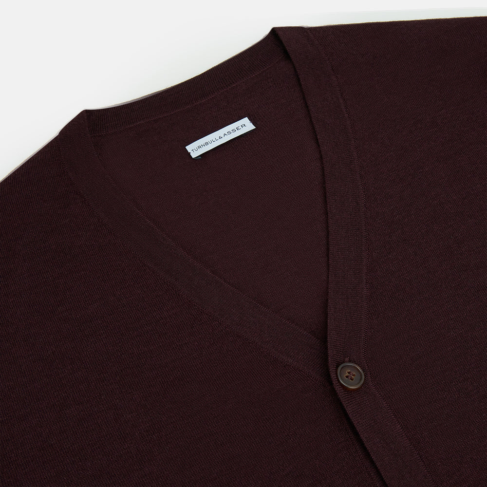 The Turnbull & Asser Burgundy Fine Merino V-Neck Cardigan features long sleeves and a button-down front, highlighting elegant handcrafted knitwear against a plain white background.