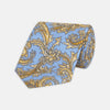 View 1 of product The Turnbull & Asser GGT92000 3062 06 OS is a rolled-up necktie with an intricate blue and yellow paisley pattern on a light blue background—a stylish accessory for any wardrobe.