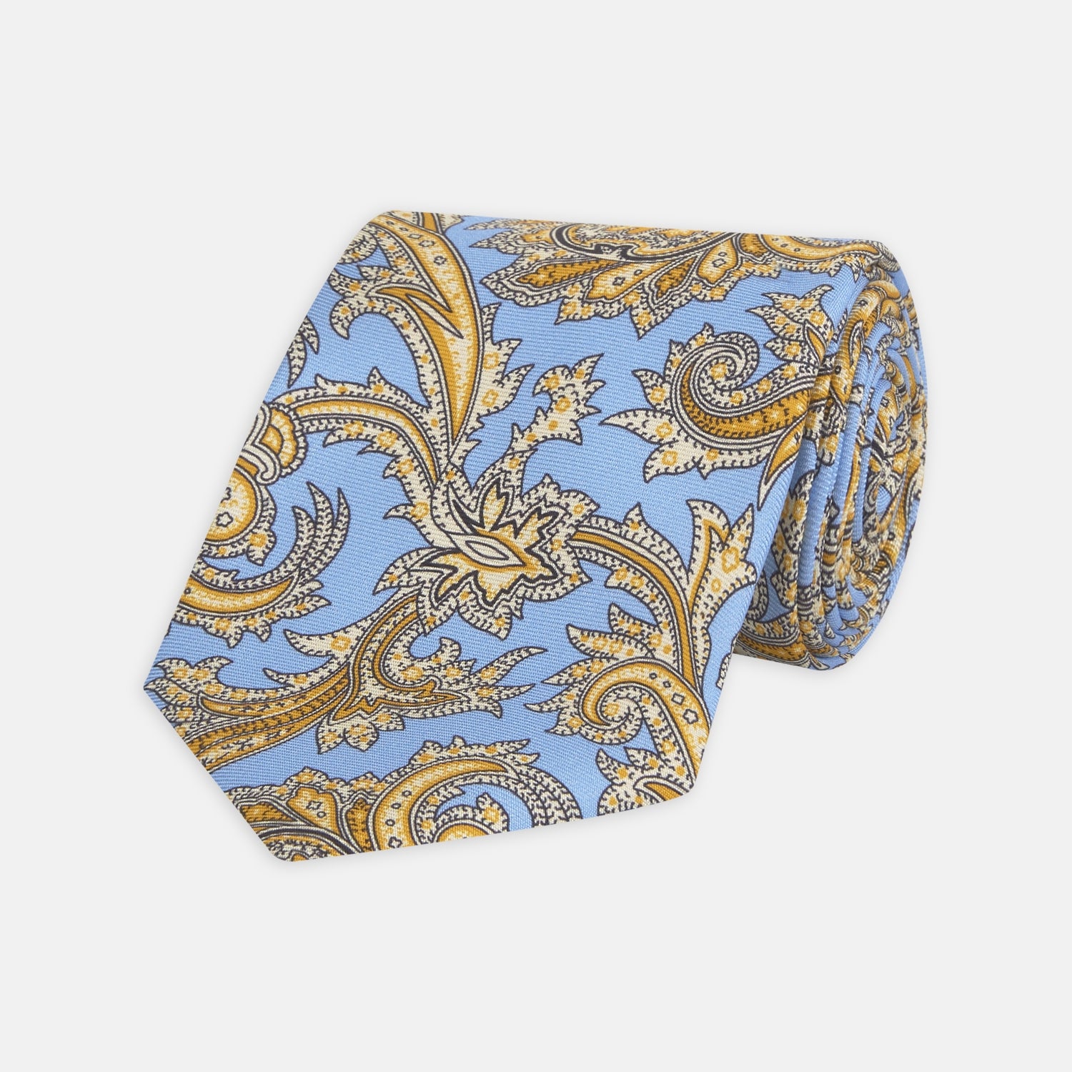 View 1 of product The Turnbull & Asser GGT92000 3062 06 OS is a rolled-up necktie with an intricate blue and yellow paisley pattern on a light blue background—a stylish accessory for any wardrobe.
