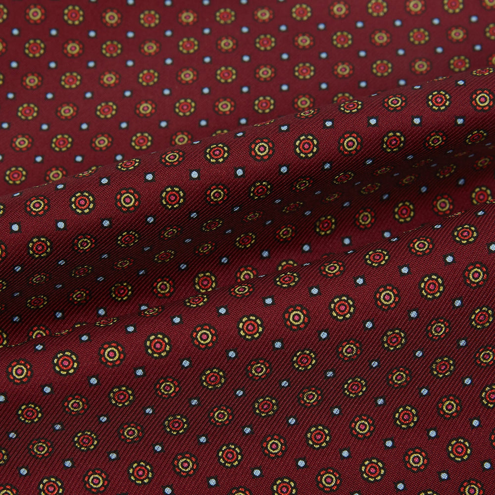 The Great Gatsby Burgundy Printed Silk Cravat by Turnbull & Asser features a maroon silk fabric with a small yellow and blue geometric pattern, subtle sheen, and neatly finished edges for an elegant, Gatsby-inspired formal accessory.