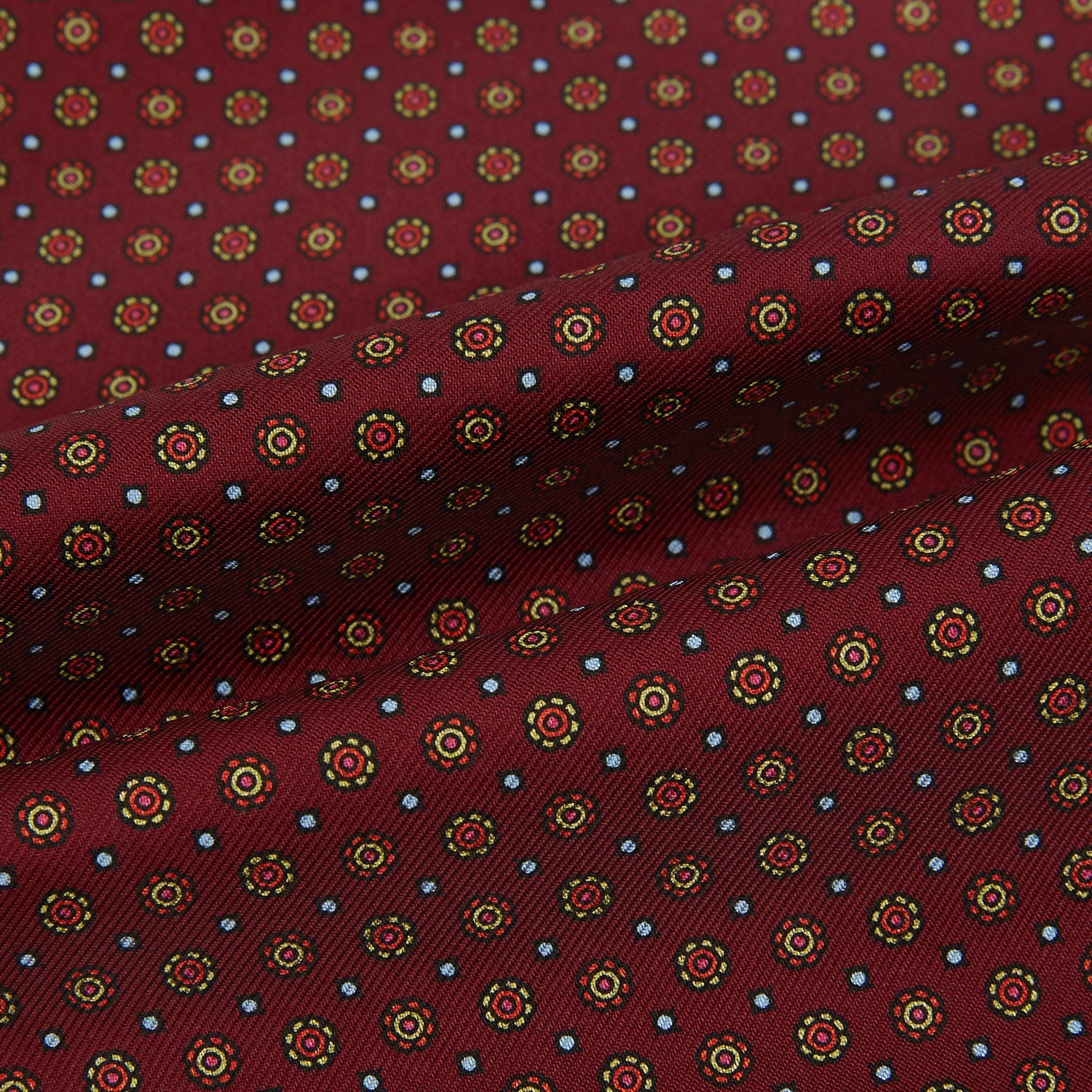 View 4 of product The Great Gatsby Burgundy Printed Silk Cravat by Turnbull & Asser features a maroon silk fabric with a small yellow and blue geometric pattern, subtle sheen, and neatly finished edges for an elegant, Gatsby-inspired formal accessory.