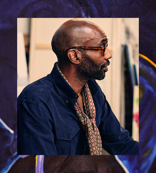 A man with a shaved head and beard, wearing glasses, a dark blue shirt, and a patterned scarf, is shown in profile against an abstract, artistic background.