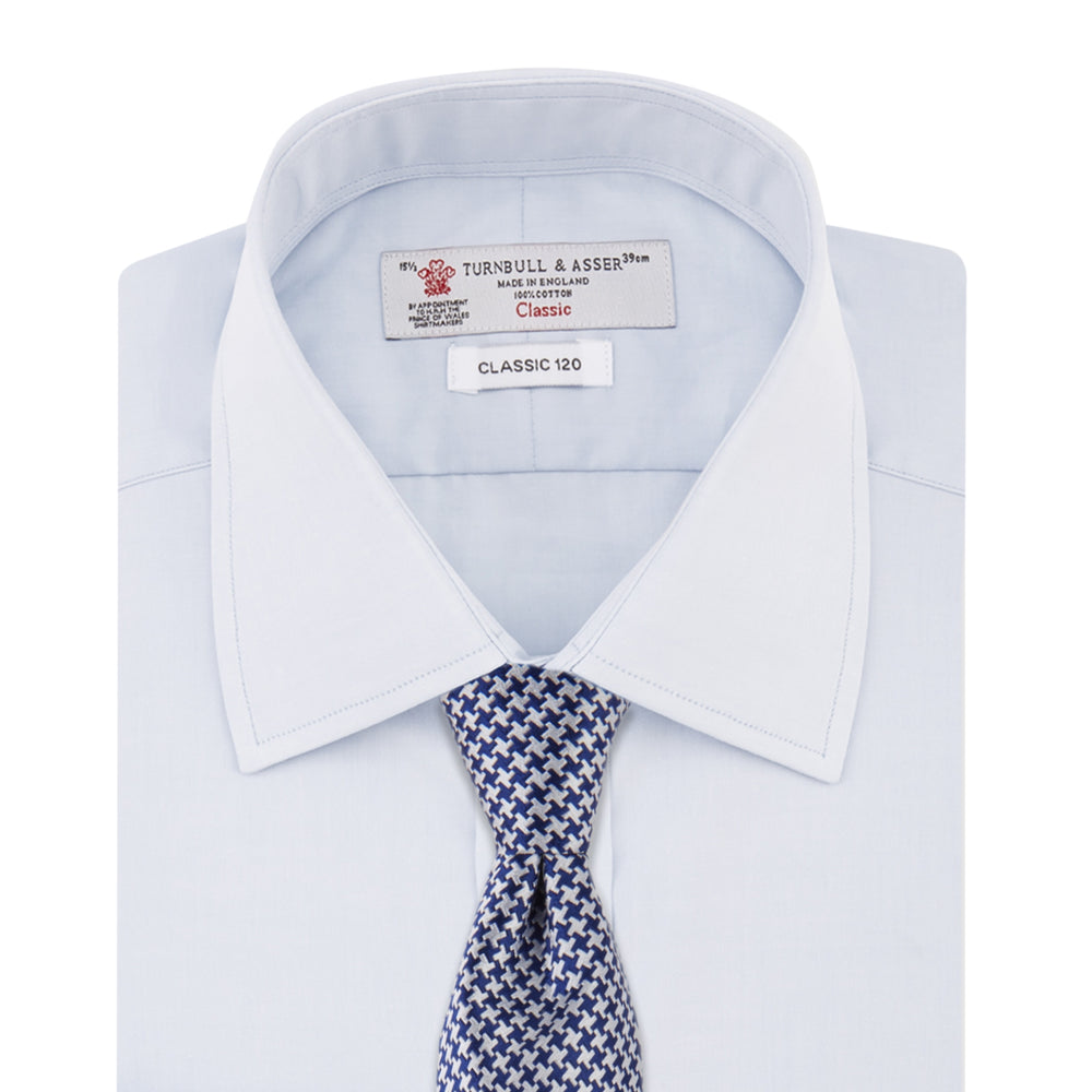 The Turnbull & Asser Two-Fold 120 Light Blue Shirt features a T&A collar, 3-button cuffs, white buttons, front pocket, and inner collar label. It is displayed neatly folded on a plain white background.