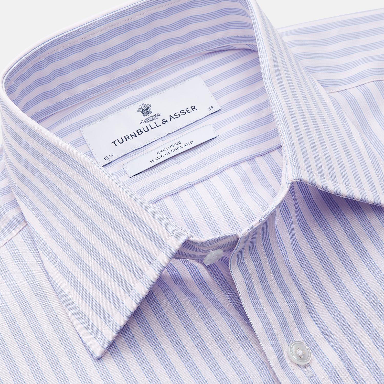 View 3 of product The Turnbull & Asser Lilac Stripe Cotton Regular Fit Mayfair Shirt features thin white and lilac stripes, a T&A collar, and buttoned cuffs, shown laid flat on a white background.