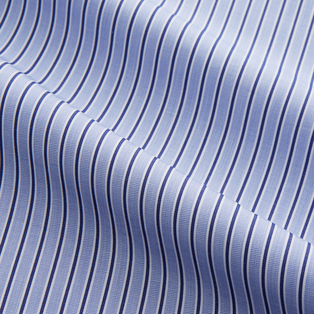 The Blue and Navy Halo Stripe Cotton Sussex Nightshirt by Turnbull & Asser features long sleeves, a collar, button-down front, chest pocket, curved hem, and brown piping for a classic luxury sleepwear style.