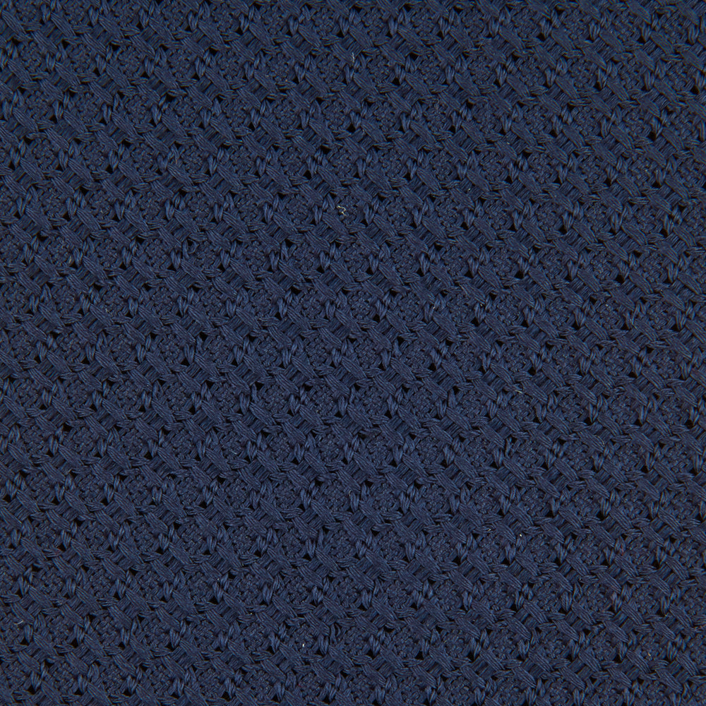 The Turnbull & Asser Navy Plain Woven Grenadine Silk Tie, an essential accessory, is rolled at one end and displayed on a plain white background.