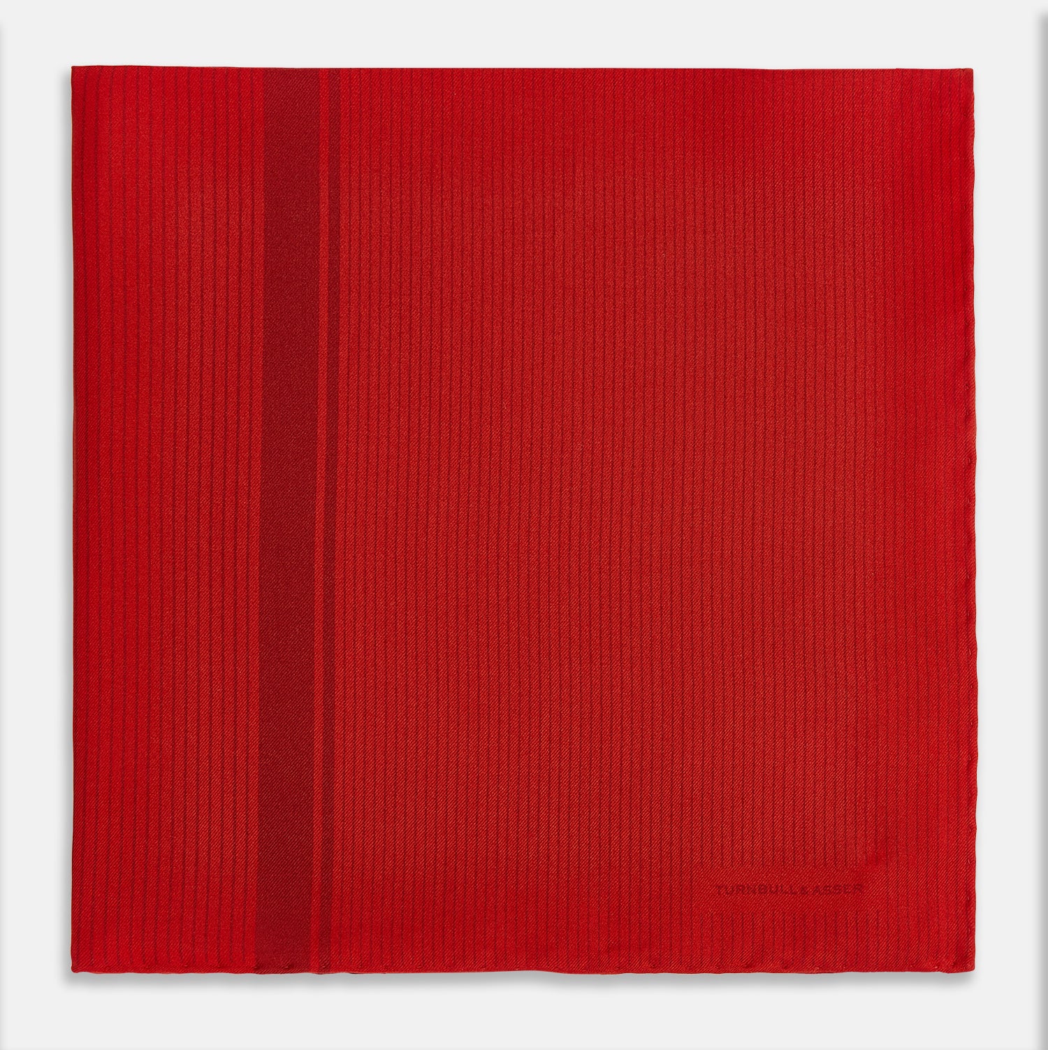View 3 of product The Red and Burgundy Stripe Silk Pocket Square by Turnbull & Asser features subtle vertical stripes and a darker red stripe along one side, with “Turnbull & Asser” embossed in the fabric and a textured, turned-down corner.