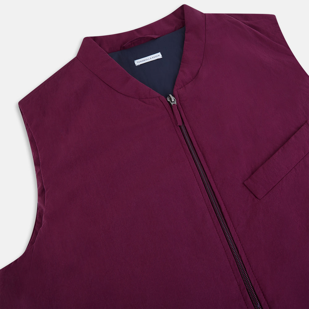 The Turnbull & Asser Wine Red Padded Gilet features a sleeveless design, front zipper, two zippered side pockets, a slanted chest pocket, and a rounded hem—perfect for the modern gentleman and shown on a plain white background.